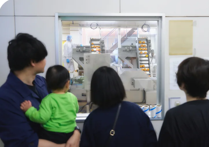 ガラス越しにジュース製造ラインを見学する親子